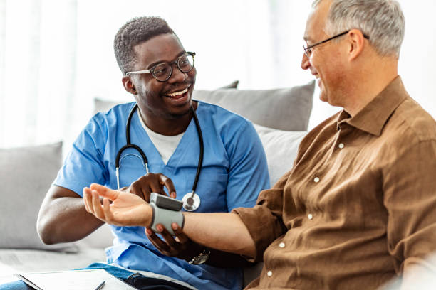 African-American Male Nurse Measuring Blood Pressure of Mature Patient in the Livingroom.